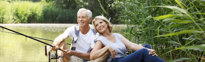 Portrait of senior couple sitting at pier while fishing at lakeside.