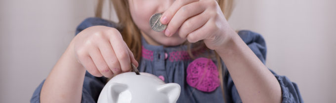 Girl adding coins to piggy bank.