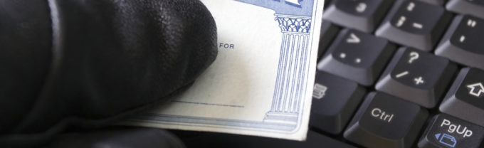 Criminal holding a social security card at a computer.